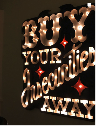 Illuminated sign sculpture: Buy Your Insecurities Away